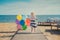 Cute blond baby girl child posing enjoying summer life time on sandy beach sea side on wooden pier with colourful plenty balloons