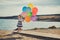 Cute blond baby girl child posing enjoying summer life time on sandy beach sea side on wooden pier with colourful plenty balloons