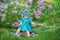 Cute blond baby girl enjoying time on a awesome place between lilac syringe bush.Young lady with basket full of flowers dressed in