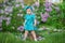 Cute blond baby girl enjoying time on a awesome place between lilac syringe bush.Young lady with basket full of flowers dressed in