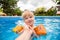 A cute blond baby girl at swimming pool with blue colored water , hold parent`s hand and fells happy.