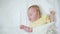 Cute blond baby sleeps lying on his back on a white bed sheet.