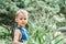 Cute blond boy stands near lush plant looking in camera