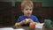Cute blond child boy sitting in wooden chair and eating big red apple fruit. Portrait on blurred background, closeup
