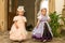 Cute blond curly twin girls dressed up as princesses in the garden of ancient castle, beautiful small girls in blue and pink long