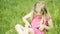 Cute blond girl in preschool age sitting in green grass playing with smart phone