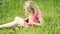 Cute blond girl in preschool age sitting in green grass playing with smart phone