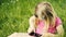 Cute blond girl in preschool age sitting in green grass playing with smart phone