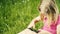 Cute blond girl in preschool age sitting in green grass playing with smart phone