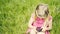 Cute blond girl in preschool age sitting in green grass playing with smart phone