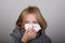 Cute blond hair little girl blowing her nose with paper tissue. Child winter flu allergy health care concept