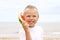 Cute blond-hared toddler smiling and holding a slice of watermelon like a phone.