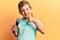 Cute blond kid singing song using microphone smiling happy and positive, thumb up doing excellent and approval sign