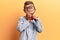 Cute blond kid wearing nerd bow tie and glasses holding magnifying glass covering mouth with hand, shocked and afraid for mistake