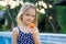 Cute blond little girl in blue swimsuit sitting at the swimming pool, eating passion fruit. Enjoy eating tropical fruit. Summer