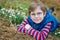 Cute blond preschool kid boy discovering first spring flowers, beautiful snowdrops