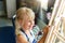 Cute blond smiling caucasian kid painting on wooden easel in class workshop lesson at art studio. Little girl holding brush in