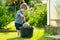 Cute blond toddler playing with a cooking pot outdoors in the garden. Kid helping parents with gardening in the backyard in bright