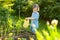 Cute blond toddler with a watering pot outdoors in the garden. Kid helping parents with gardening in the backyard in bright sunny
