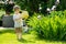 Cute blond toddler with a watering pot outdoors in the garden. Kid helping parents with gardening in the backyard in bright sunny