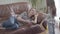 Cute blond woman lying on the leather sofa talking by cell phone. Little girl pulls her mother hand, she needs attention