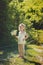 Cute blond young girl child stylish dressed in white shirt wearing wreath of daisy chamomiles posing on meadow of forest wild mayw