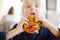 Cute blonde boy eating large hamburger at fastfood restaurant. Unhealthy meal for kids. Junk food