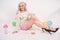 Cute blonde caucasian happy girl dressed in a milky color knitted sweater and funny shorts, she sits on the white floor alone with