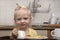 Cute blonde child with cup in hands in kitchen. Breakfast with child. Little girl drinks a milk