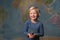A cute blonde child holds a seedling in front of a world map
