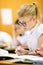 Cute blonde school student with stylish glasses writing in classroom