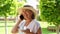 cute blonde senora woman, 50-55 years old, in a hat and a white dress, talks using a smartphone and holds a cup of