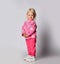 Cute blonde smiling baby kid girl in pink warm fleece clothing with heart print pattern stands side looking at camera