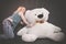 Cute blonde teen in jeans and plaid shirt plays with her huge Teddy polar bear in yellow scarf on black background