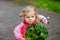 Cute blonde toddler girl planting seeds and seedlings of geranium flowers in garden. Happy healthy baby child on cold