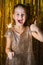 Cute blonde toddler girl wearing fancy hold burning sparkler against golden glitter background and emotionally smile