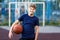 Cute boy in blue t shirt plays basketball on city playground. Active teen enjoying outdoor game with orange ball. Hobby