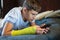Cute boy with broken hand relaxing and smiling on couch. Close up young handsome Teenage with elbow plaster playing smartphone
