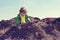 Cute boy with curly blond hair playing above pile of earth wearing green clothes and yellow scarf