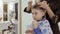 Cute boy drinks cocktail during hairdresser cuts his hair in barbershop