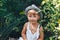 Cute boy in hat and casual clothes sitting around tomatoes ang looking at camera, kid model posing in garden