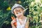 Cute boy in hat and casual clothes sitting around tomatoes ang looking at camera, kid model posing in garden