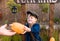 A cute boy in a hat sells pumpkins at a wooden counter