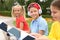 Cute boy in headphones and girls reading books in park