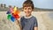 Cute boy holding colorful spinning pinwheel on sandy sea beach. Concept of summer holiday, happiness, joy, travel and weekend