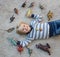 Cute boy lies on light carpet on his back. There are many dinosaur figures spread out around it