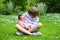 Cute boy sitting in a beautiful summer garden full with flowers holding his newborn sister