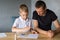 A cute boy is sitting with his dad at the table and collecting origami. Adds up the details