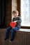 Cute boy sitting on wooden window sill with red box in shape of heart. Valentines day or kids healthcare, medical