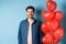 Cute boyfriend looking happy and smiling, standing near Valentines day heart balloons on blue background